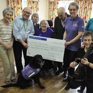 Mungo at Colten Care’s Linden House care home in Lymington with his partner Barbara Houston, seated. Also joining residents and team members are Canine Partners volunteer Liz Downs, standing third from right, and singer and guitarist Nigel Revill.